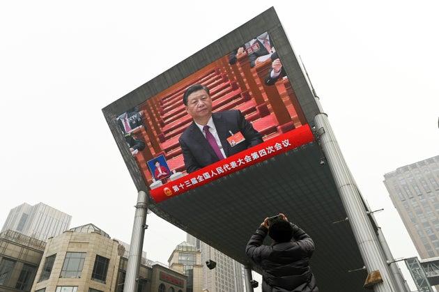 A man uses his mobile phone to take a picture of a big screen showing China's President Xi Jinping attending...