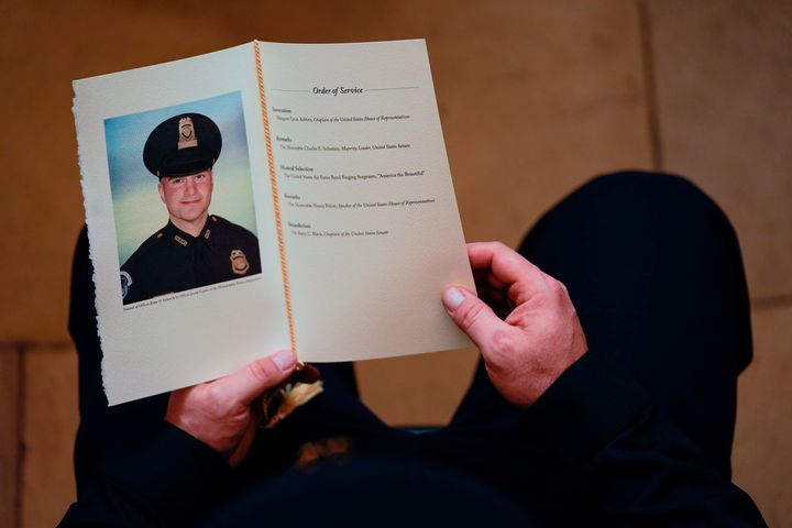 An officer holds a program as people pay their respects at the remains of U.S. Capitol Police officer Brian Sicknick.