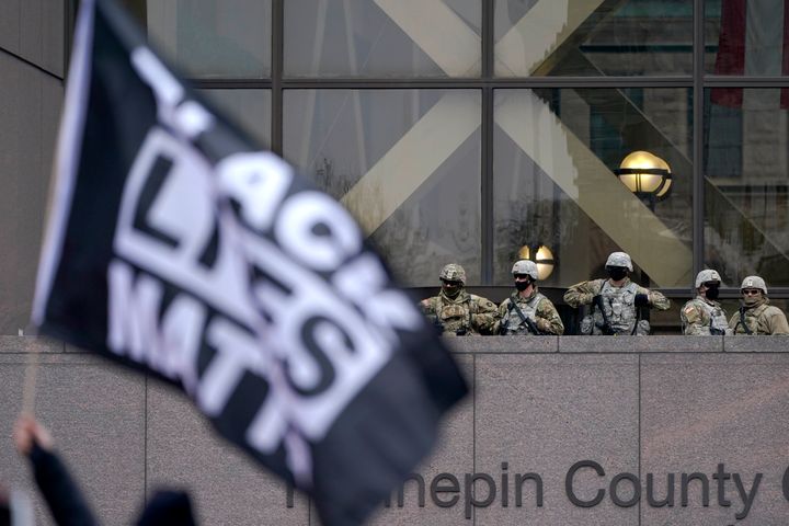 National Guard members are seen as a person flies a Black Lives Matter flag during a rally outside of the Hennepin County Government Center in Minneapolis on Monday, April 19, 2021, after the murder trial against former Minneapolis police Officer Derek Chauvin advanced to jury deliberations. (AP Photo/Julio Cortez)
