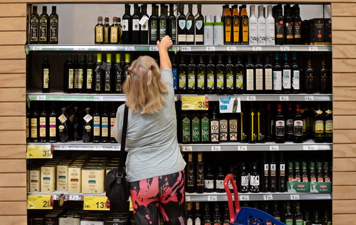 Mujer coge botella de aceite de oliva virgen extra de una estantería del supermercado.