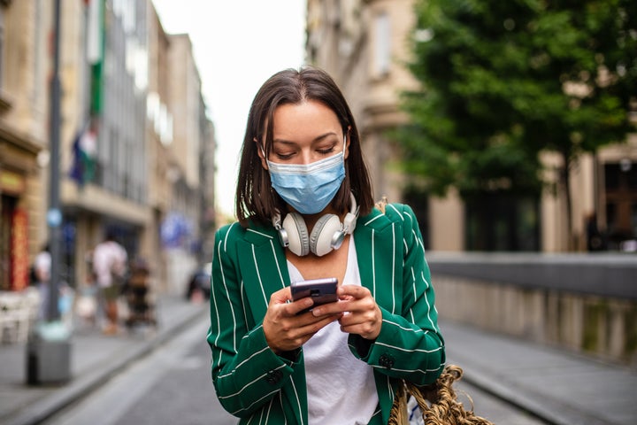 Una mujer maneja su teléfono por la calle mientras lleva una mascarilla.
