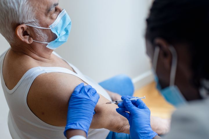 African-American, female injecting COVID-19 vaccine to a senior man. Shallow DOF, focus on a foreground