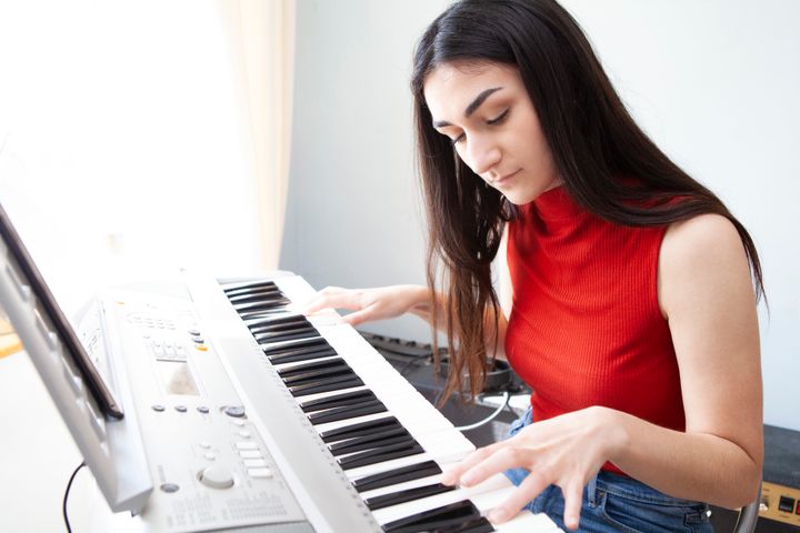 Young woman sitting at piano and learning to play