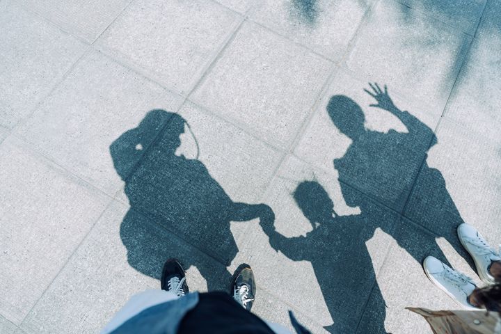 Shadow on gravel path of a loving family of three holding hands walking outdoors on a lovely sunny day