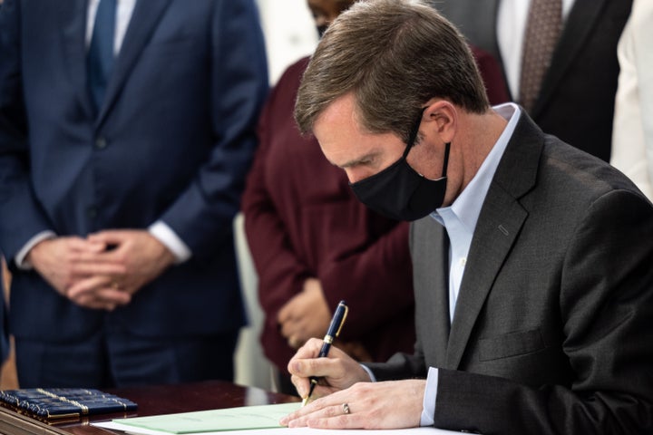 Kentucky Gov. Andy Beshear signs a bill while surrounded by its sponsors during a bill signing event at the Center for Africa