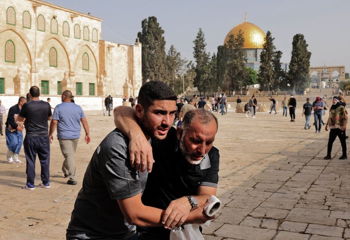 A Palestinian man helps a wounded fellow protester amid clashes with Israeli security forces at Jerusalem's Al-Aqsa mosque co