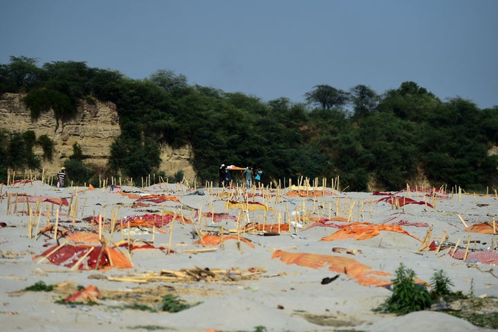 Relatives carry a dead body past shallow graves covered with saffron cloth on the banks of the Ganges River in Shringverpur village on Saturday.