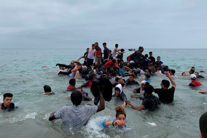 Un grupo de personas se hacen con una embarcación de las autoridades marroquíes en la playa de la localidad de Fnideq (Castillejos) para cruzar los espigones de Ceuta este martes en una avalancha de inmigrantes sin precedentes en España al registrarse la entrada en 24 horas de 5.000 personas (un tercio de ellas menores).