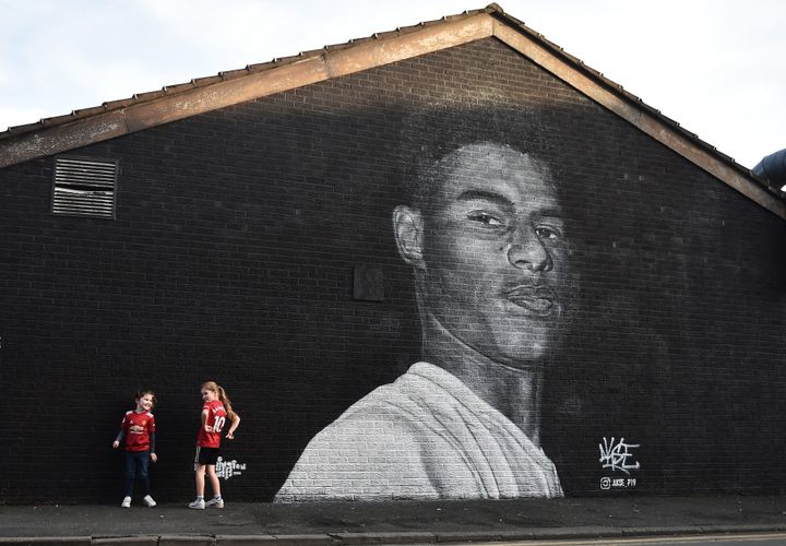 Two young girls pose for a photograph at a mural of Manchester United footballer and child poverty campaigner Marcus Rashford