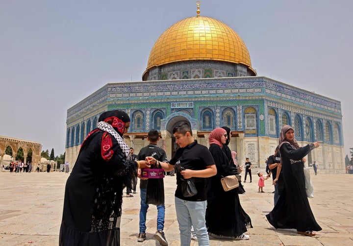 A Palestinian woman offers sweets to worshippers to celebrate the end of fighting between Israel and Hamas, during Friday pra