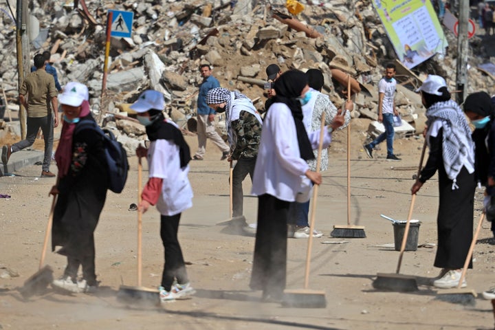 Des volontaires palestiniens balaient les décombres des bâtiments, récemment détruits par les frappes israéliennes, dans le quartier de Rimal à Gaza le