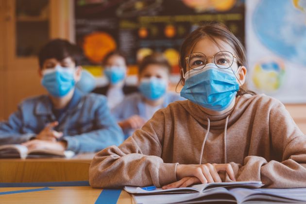 High school students at school, wearing N95 Face masks. Teenage girl wearing eyeglasses sitting at the school desk and listening to the teacher.