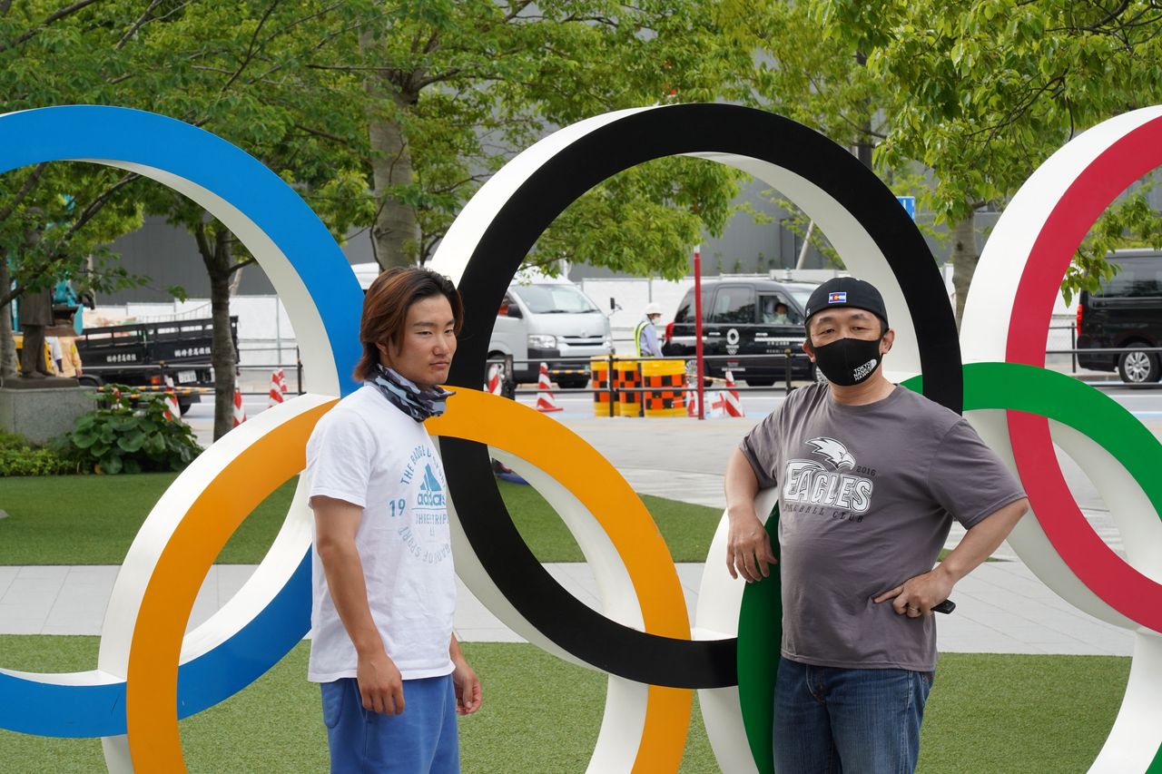 3 Ιουνίου 2021. Δύο νεαροί Ιάπωνες ποζάρουν μπροστά στους εμβληματικούς κύκλους των Ολυμπιακών Αγώνων στο Τόκιο. Ενας με μάσκα και ένας άνευ. Κάτι σαν αληγορική εικόνα... (Photo by Jinhee Lee/SOPA Images/LightRocket via Getty Images)