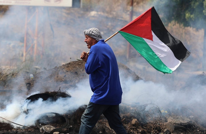 A Palestinian protester lifts a national flag amid confrontations with Israeli security forces at the Hawara checkpoint south of Nablus city, in the occupied West Bank, on May 21, 2021, following demonstrations in support of Palestinians in Jerusalem's Sheikh Jarrah and the Gaza Strip. (Photo by JAAFAR ASHTIYEH / AFP) (Photo by JAAFAR ASHTIYEH/AFP via Getty Images)