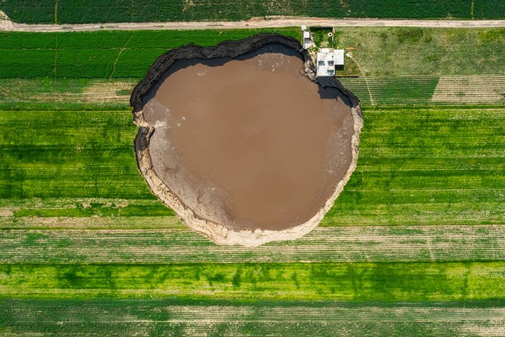 The large sinkhole that appeared in late May at a farm in central Mexico has grown larger than a football field, begun swallowing a house and trapped two dogs in its depths. 