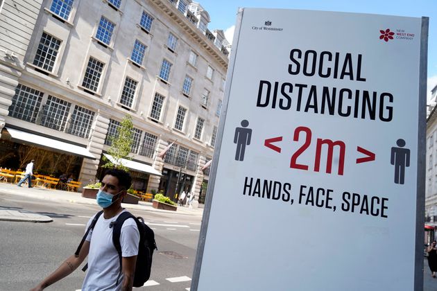 Un passant portant un masque devant un panneau demandant aux personnes de respecter les mesures de distanciation à Londres le 7 juin. 