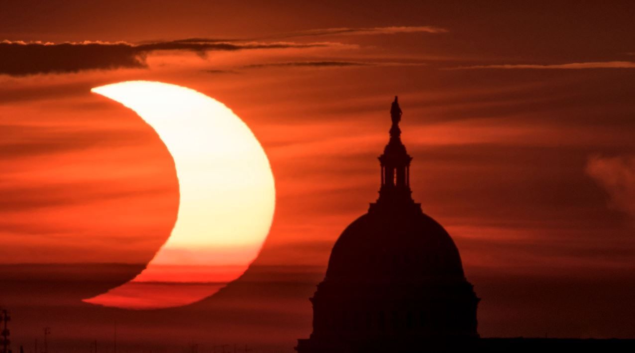 Μια μερική ηλιακή έκλειψη με τον ήλιο να ανατέλλει στα αριστερά του Καπιτωλίου των Ηνωμένων Πολιτειών στην Ουάσιγκτον στις 10 Ιουνίου, όπως φαίνεται από το Άρλινγκτον της Βιρτζίνια, μέσα από τον φακό της NASA.