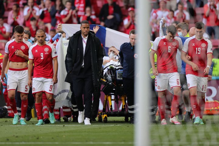 Denmark's players escort Eriksen off the field.