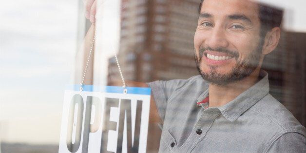 Mixed race man placing Open sign in shop window