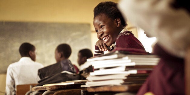 A Happy young South African girl (from the Xhosa tribe) works on her studies and jokes with her friends at at an old worn desk in a class room in the Transkei region of rural South Africa.