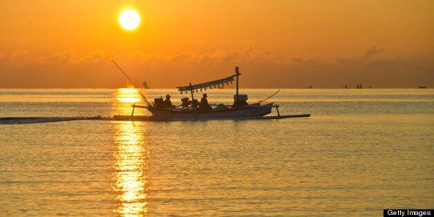 Catamaran (Jukung) of Bali / Indonesian fisherman at sunrise is coming home. With lamps on the boat for fishing in the night
