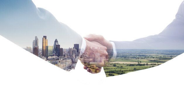 A double exposure of two business men shaking hands with a view of the City of London and of a green fields landscape.