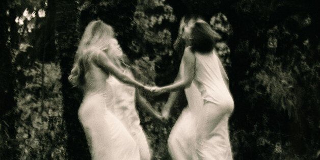 Four young women dancing in forest, holding hands (B&W, blurred motion)