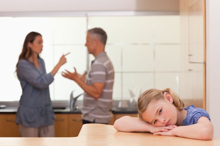 Sad little girl listening her parents having an argument in a kitchen