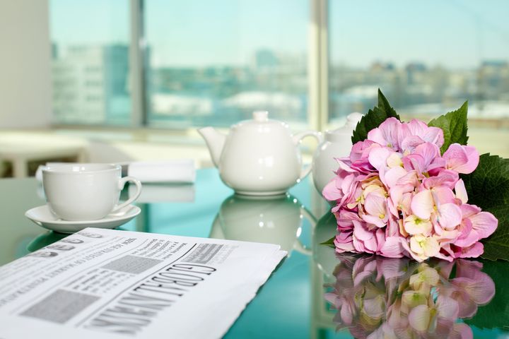Table with porcelain cup and pot, newspaper and bunch of flowers on it