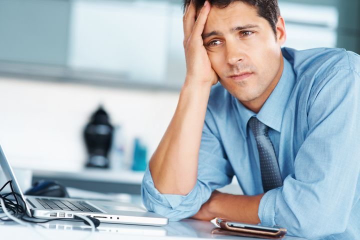 Businessman sitting at desk with hand on his face, looking worried