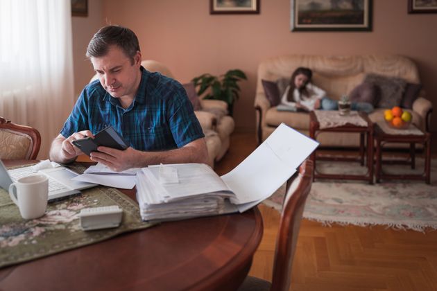 Serious man using smart phone when calculating expenses