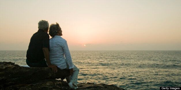 mature couple sitting on rock watching sunset over sea