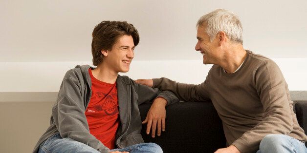 Mature man with his son sitting on a couch and gossiping