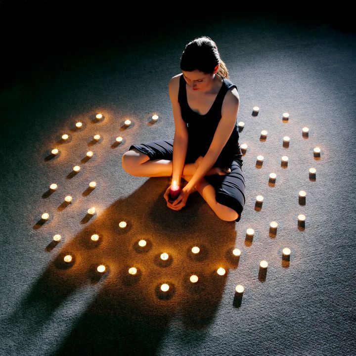 Mid adult woman sitting cross-legged on carpet surrounded with lit candles
