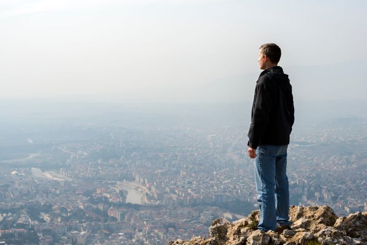 A man standing on a peak, looking over a city and the river running through it. Location: Antakya, Turkey
