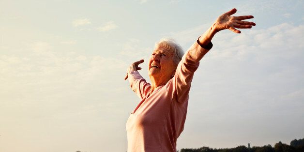 senior woman, 88 years old, very active and flexible, stretching her arms at a lake at a sunny summer morning