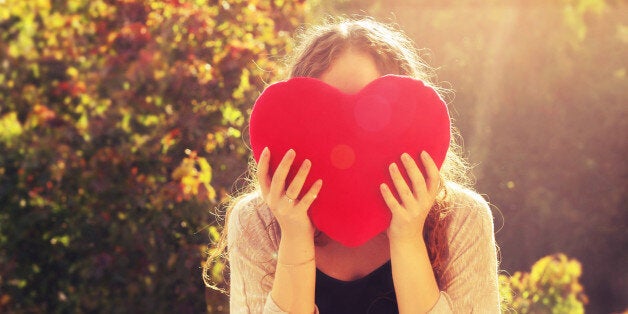 A girl holding up a heart in golden hour.