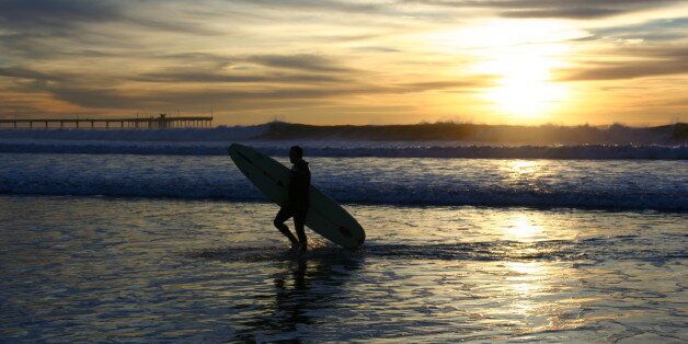 surfer walks out of water at sunset