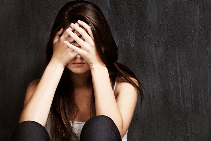 A studio shot of a sad young woman holding her head in her hands