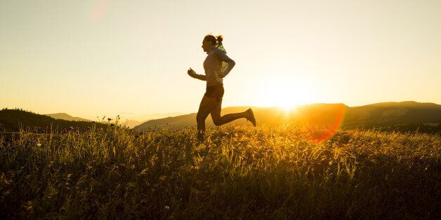 A woman trail running at sunset through a golden field of grass.