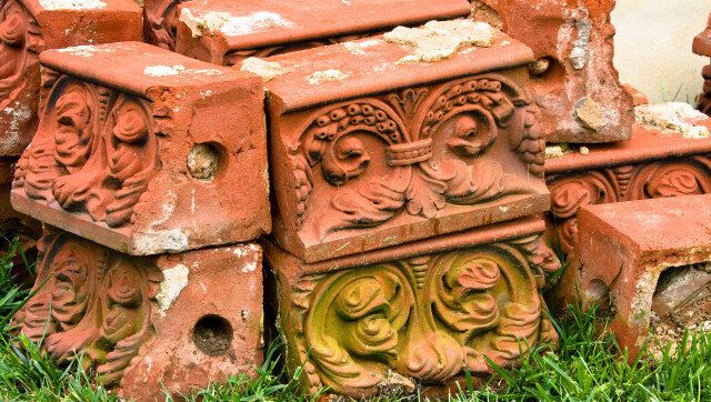 Antique decorative molded bricks salvaged from demolished building stacked on grass.