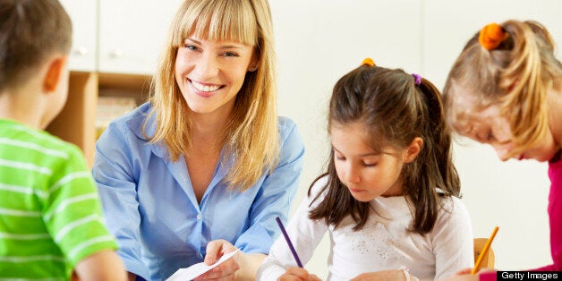 Preschool: Young smiling teacher drawing and coloring with group of children. Learning and having fun. Selective focus to teacher looking at camera and smiling.