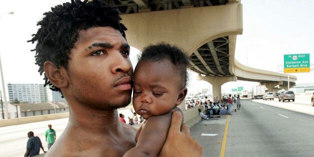 NEW ORLEANS - AUGUST 31: Daryl Thompson holds his daughter Dejanae, 3-months, as they wait with other displaced residents on a highway in the hopes of catching a ride out of town after Hurricane Katrina August 31, 2005 in New Orleans, Louisiana. Thompson and thousands of others were looking for a place to go after leaving the Superdome shelter. (Photo by Mario Tama/Getty Images)