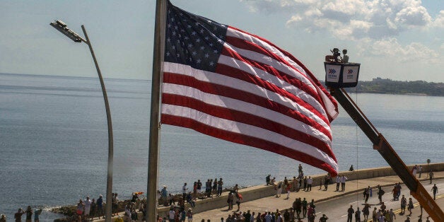 In this photo taken through a window, Cuban videographers film the U.S. flag from a crane after it was raised at the U.S. Embassy in Havana, Friday, Aug. 14, 2015. The Stars and Stripes rose over the newly reopened U.S. Embassy after a half-century of broken diplomatic relations. (AP Photo/Ramon Espinosa)
