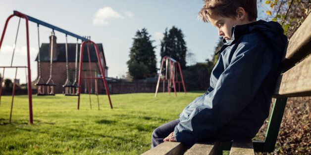 Upset problem child sitting on play park playground bench concept for bullying, depression, child protection or loneliness