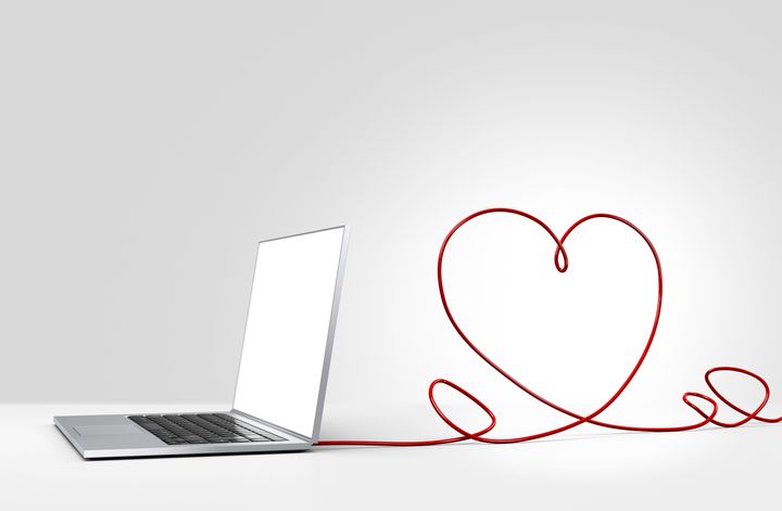 Laptop computer with a red ethernet cable forming a heart, coming out of the back on a plain background
