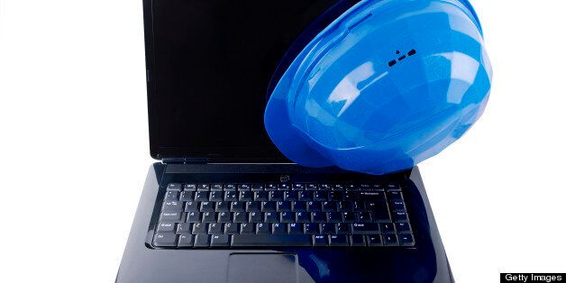 Shiny black laptop with blue safety helmet hanging from the corner of the screen.
