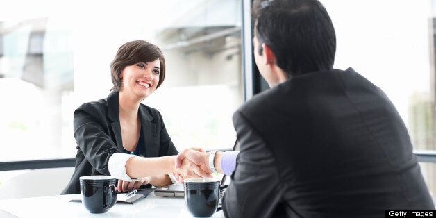 Friendly businesswoman smiles and shakes hands with a businessman across the table. Copy space over windows. CLICK FOR SIMILAR IMAGES AND LIGHTBOX WITH MORE BUSINESS PEOPLE. 