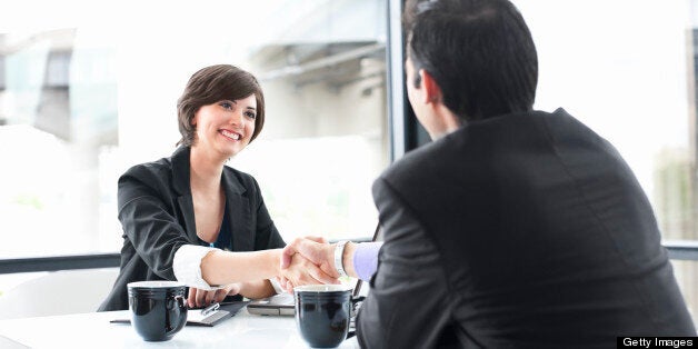 Friendly businesswoman smiles and shakes hands with a businessman across the table. Copy space over windows. CLICK FOR SIMILAR IMAGES AND LIGHTBOX WITH MORE BUSINESS PEOPLE.