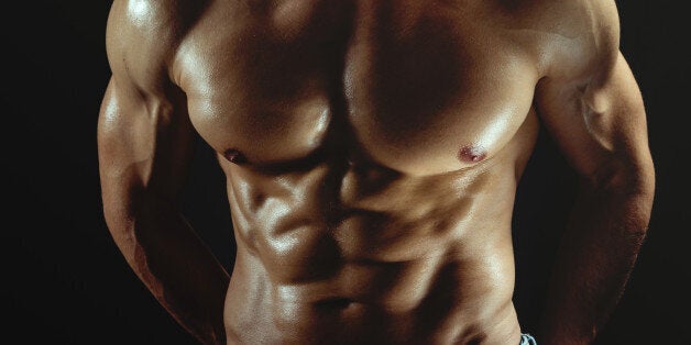 Strong shirtless man with great body posing in front of dark background. Studio shoot.